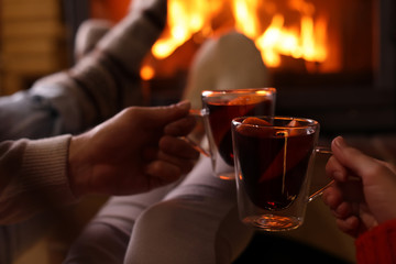 Couple with mulled wine near fireplace indoors, closeup. Winter vacation
