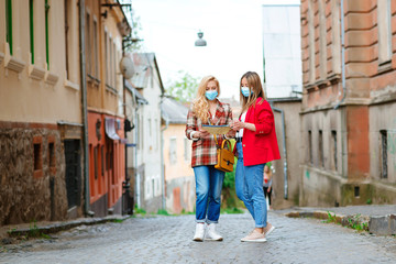 Fototapeta na wymiar Summer vacation after coronavirus lockdown. Tourists girls wearing face masks at street.