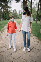 Obraz premium Portrait of mother and child with antivirus masks walking on park alley. Woman holding little girl's hand while wearing medical masks and walking in park.