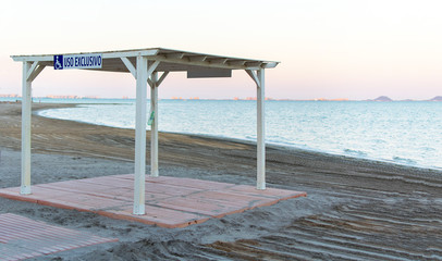 Fototapeta na wymiar Arbor for Wheelchair user exclusive use at Los Narejos beach in Spain. Places in the Beach for people with disabilitiesthe sign is blue on a white background for the disabled to see it.
