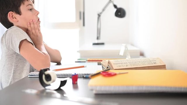 Stress kid doing homework.Boy at study table doing homework with stress action.Lazy boy doing homework with stressed face.