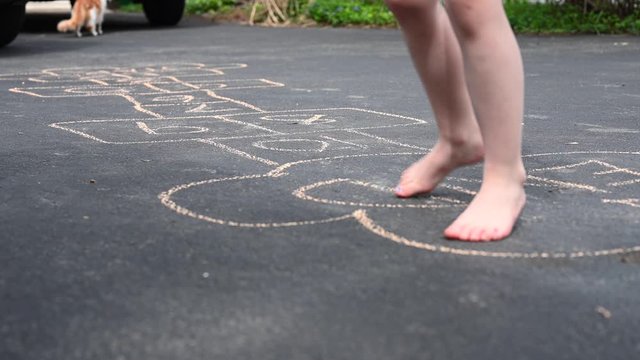 barefoot little girl playing hopscotch game in driveway at home with cat