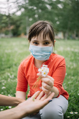 Cute girl with antivirus mask holding fresh bouquet. Portrait of child with medical mask gathering flowers and camomile from meadow and holding bouquet.