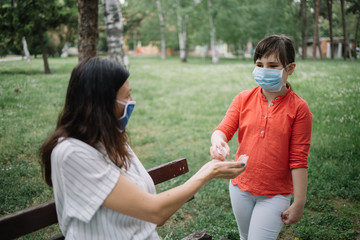 Cute girl disinfecting mother's hands with antiseptic spray. Little girl wearing antivirus mask holding disinfectant over woman's hands to prevent spreading of the coronavirus.