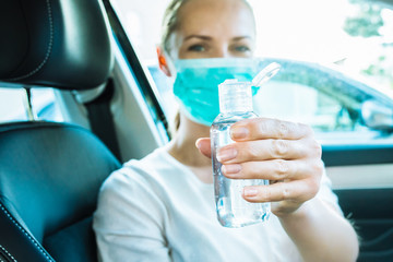 Young woman using hand sanitizer to disinfect her hands while driving a car during coronavirus outbreak. Virus prevention. Covid-19 background with copy space.