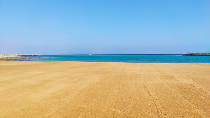 Fototapeta na wymiar Deserted seashore. Yellow sand and blue water of the sea.