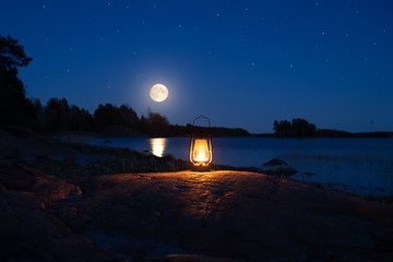 Vintage lantern in forest on shore of lake. Oil lamp with warm orange light on the rock. Beautiful...