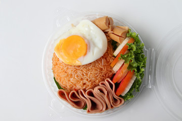 Fried rice with fried egg, bacon and vegetables In a round plastic box isolated on white