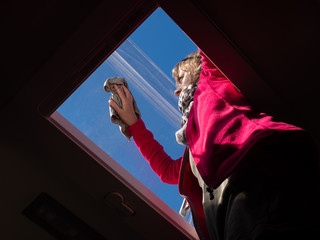 Viewed from below a lady cleans her skylight window of her recreational vehicle with blue sky and sunshine highlighting her contrasting with dark interior.Image