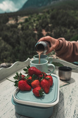 Close-up of picnic food: delicious fresh strawberries and coffee. Female hand pours coffee to cup from thermos.