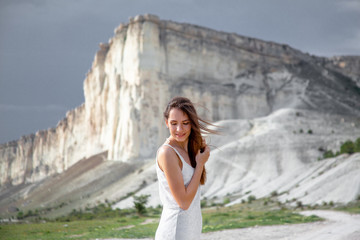 alone woman walking in the beautiful place. Female dressed white drss and posing against the white mountain cloudy sky