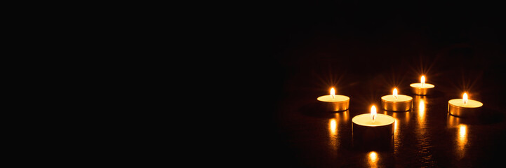 Fototapeta na wymiar Several burning candles on a black background. Banner with copy space.