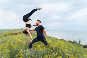 Couple practicing acro yoga poses outdoors outside. Pair of sportsmen acrobats showing flexibility class workout. Athlete holding girl, that doing upside down. Woman holding her body with muscles