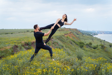 Young couple practicing acroyoga on mat in gym together. Woman stretching and balancing on man legs. Partner yoga, flexibility, trust concept, copy space