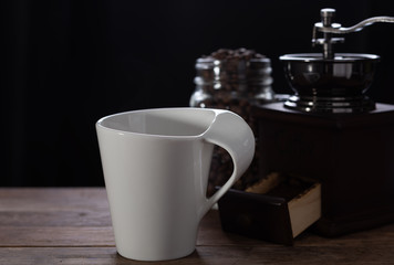 White coffee cup,coffee grinder and roasted beans on wooden table with dark background