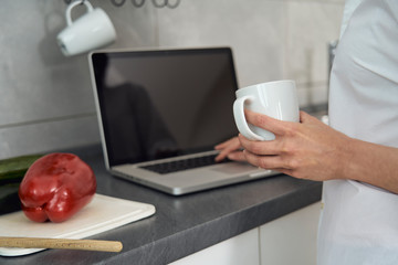 Woman food blogger who takes care of health cooking spaghetti with vegetables by publishing updates with laptop pc in your kitchen on blogs and online social networks
