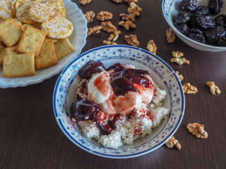 the cottage cheese mixed with sour cream, jam, nuts and crackers with prunes in a light-coloured dishes on a dark table