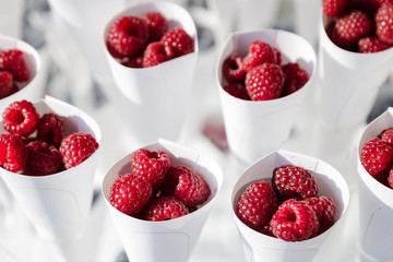 Ripe beautiful red raspberries in white glasses. White packaging. Ripe raspberry berries in summer.
