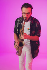 Young caucasian jazz musician playing the saxophone on gradient pink studio background in neon light. Concept of music, hobby, festival. Joyful, cheerful attractive guy. Colorful portrait of artist.