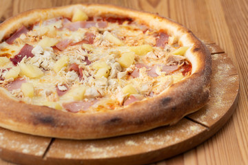 hearty italian pizza on a wooden board. pizza with ham, chicken and pineapple