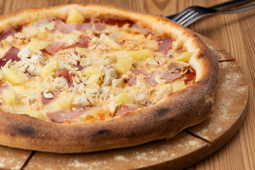 hearty italian pizza on a wooden board. pizza with ham, chicken and pineapple