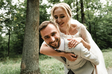 the bride gently hugs the groom from the back and happily whispers in his ear the kind words on the wedding day,Wedding couple. Happy bride with wedding bouquet holds the groom's arm. Stylish 