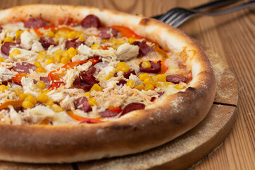 hearty italian pizza on a wooden board. crispy cheese pizza with hunting sausages, pepper, chicken and corn