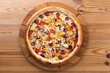 hearty italian pizza on a wooden board. crispy cheese pizza with hunting sausages, pepper, chicken and corn