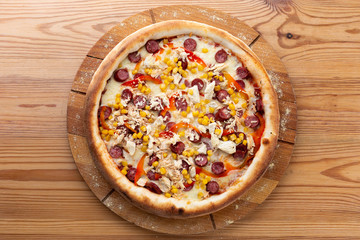 hearty italian pizza on a wooden board. crispy cheese pizza with hunting sausages, pepper, chicken and corn