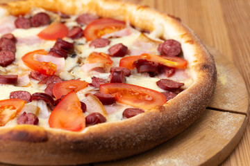 hearty italian pizza on a wooden board. .crispy cheese pizza with hunting sausages, tomato and ham