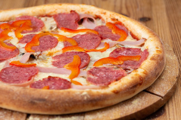 hearty italian pizza on a wooden board. .pizza with salami, fresh pepper and ham