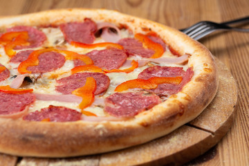 hearty italian pizza on a wooden board. .pizza with salami, fresh pepper and ham