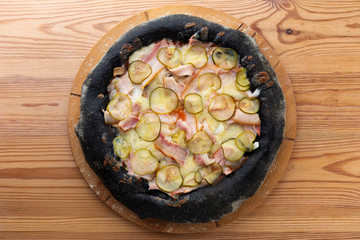 hearty italian pizza on a wooden board. .black crispy cheese pizza with ham, selensi cucumbers and mushrooms