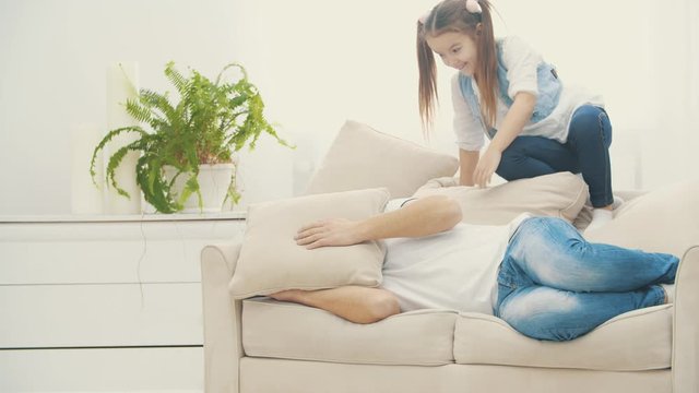 4k video where daughter jumps onto a sofa to her dad and begs to play with.