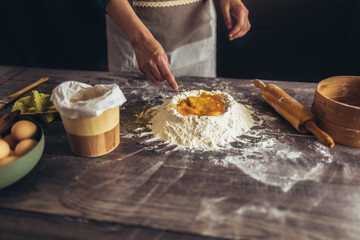 Hands whipping eggs into raw dough on wooden table.Ingredients for italian homemade pasta