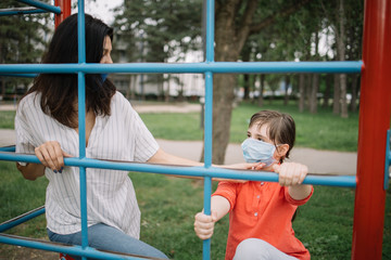 Obraz premium Careful woman fixing position of medical mask on girl's face at playground. Mother and daughter protecting their faces with antivirus masks while playing in the park.