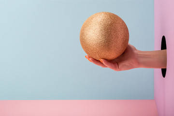 Woman's hand holding a golden glitter ball on pink and blue background