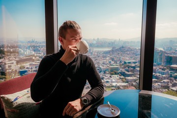 Man drinks coffee with city on background