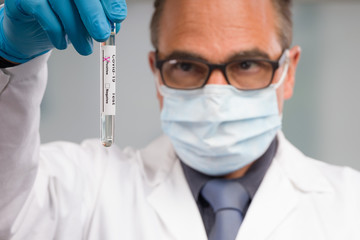 Scientist or doctor with medical face mask and medical gloves is handling virus test tube with result markers in front of laboratory in background