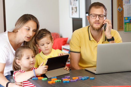 famiglia gioca con il tablet mentre il pap&agrave; lavora al telefono con i computer di fronte