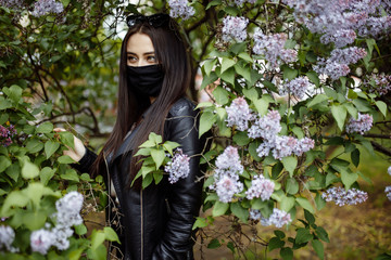 Girl in a medical mask on the background of a blossoming lilac in the park. Black mask. Coronavirus protection. Spring allergy