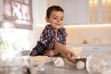 Cute little boy cooking dough in kitchen at home