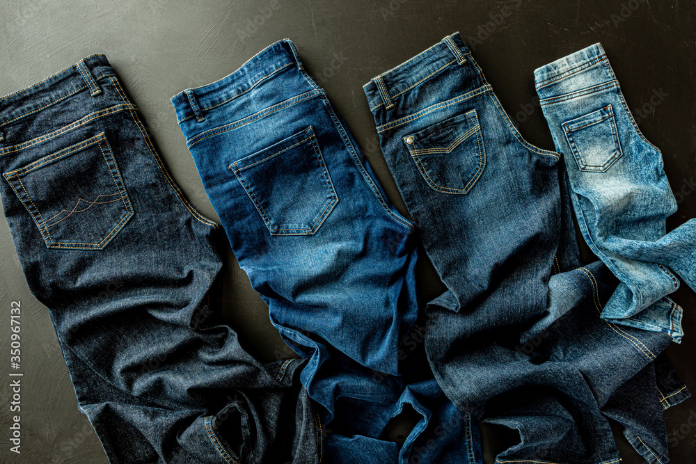 Wall mural Clothing - family jeans on black. Various denim trousers from above.