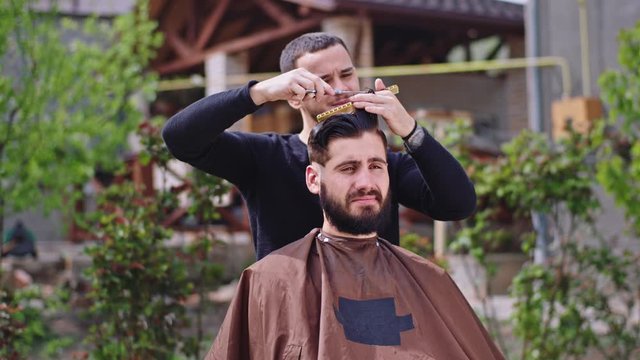 Good looking guy sitting on the garden at home he have a haircut time doing by professional barber man they discussing together