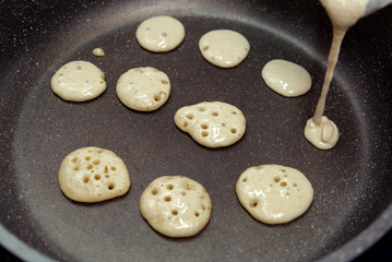 Process of cooking tiny pancake cereal - trendy quarantine food. Dough is poured into hot pan and mini pancakes are baked. Homemade breakfast.