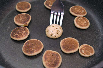 Process of cooking baked tiny pancake cereal - trendy quarantine food. Use fork to flip mini pancakes to other side on hot pan. Homemade breakfast.