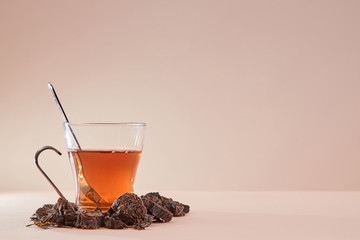 Cup made of glass filled with tea. Tea infusion around mug. Copy space. Pink background. Aromatic herbal tea concept
