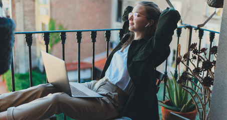 Charming happy woman sitting relaxed on balcony at home with closed eyes dreaming about summer vacation, Millennial girl working remotely from home thinking about positive things resting at workplace