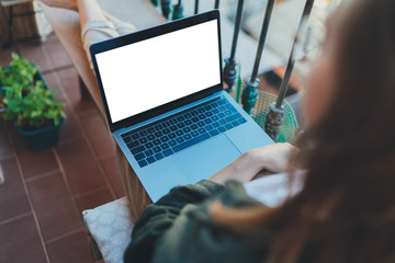 Mock up of portable computer, Young woman sitting on the balcony using laptop computer with blank screen with copy space for design or text message