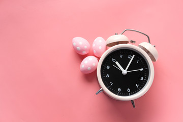 easter concept with alarm clock and eggs on pink background.